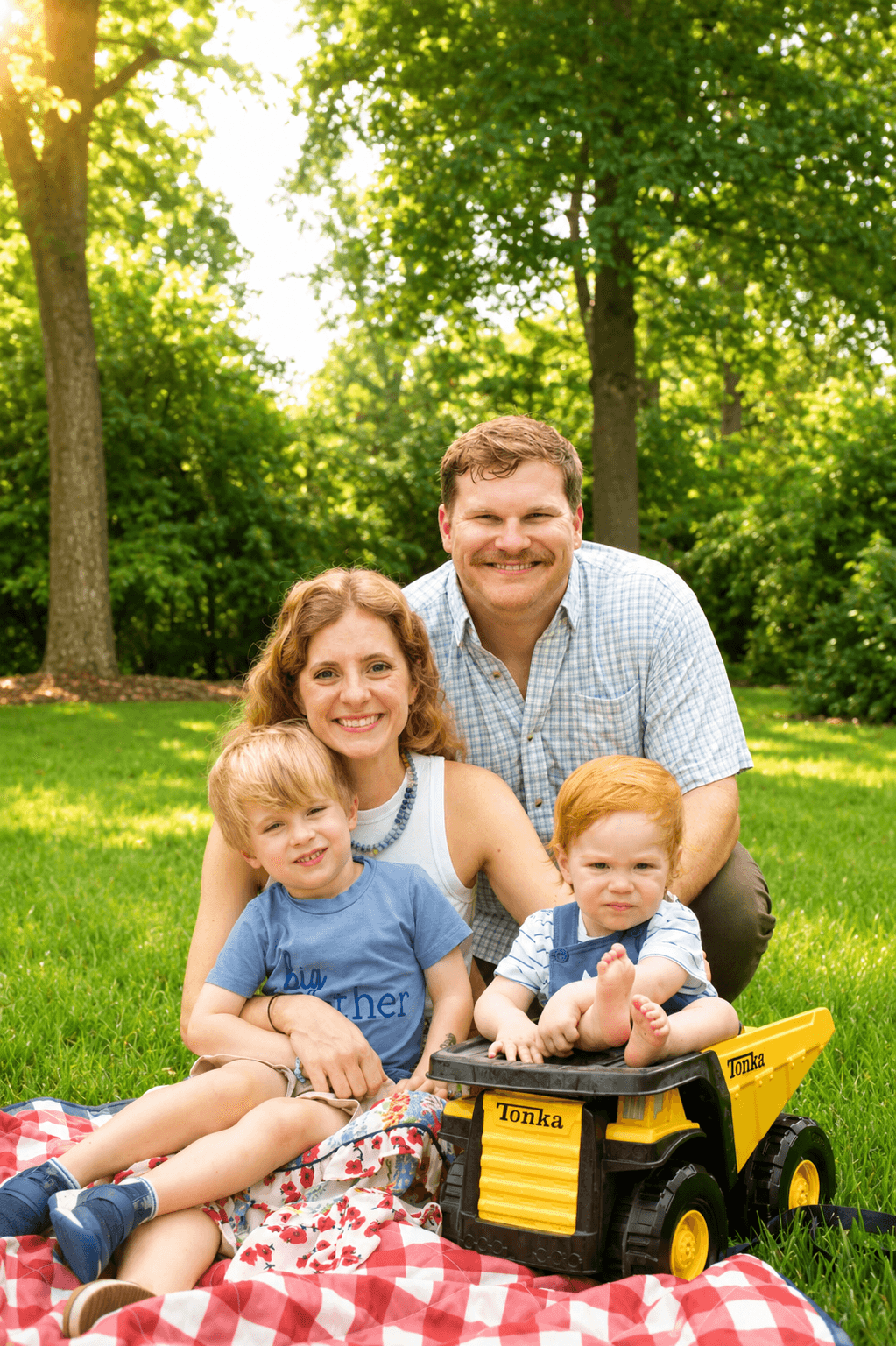Family of four smiling on a picnic blanket with a yellow toy truck