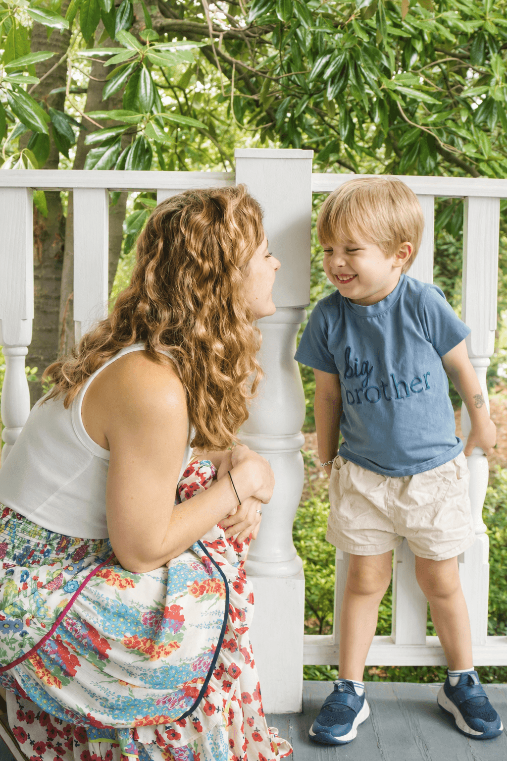 Mother and young son smiling at each other beside a white porch railing
