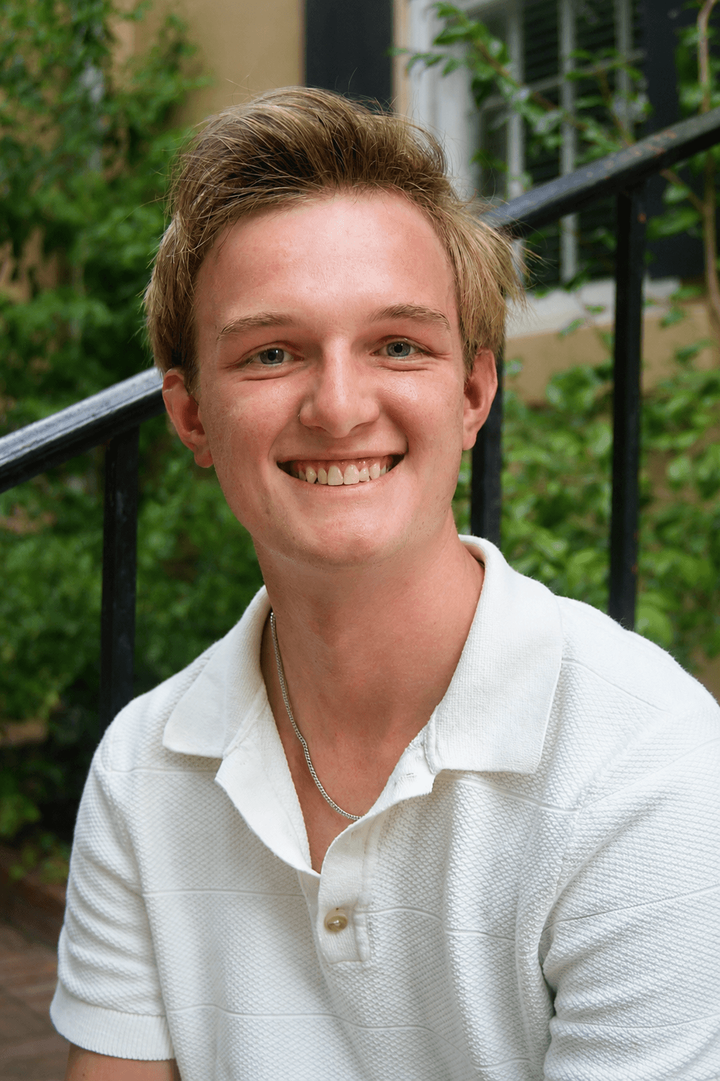 Casual outdoor headshot of a smiling man in a white shirt